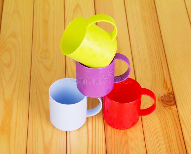 Four different color plastic mugs on background of light wood.