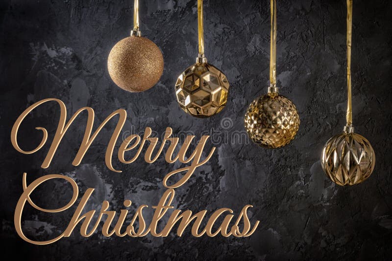 Four golden Christmas balls hanging on ribbons. Next to the inscription Merry Christmas on a black textured background. stock images Four golden Christmas balls hanging on ribbons. Next to the inscription Merry Christmas on a black textured background. stock images