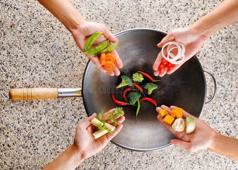 Four Hands Puts Fresh Vegetables in the Wok. Cooking Concept Stock