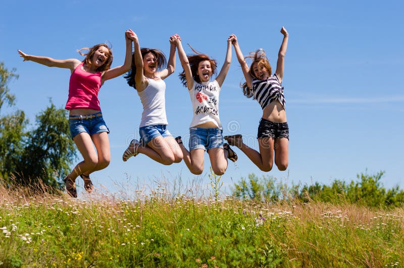 Four happy young women girls friends jumping high against blue sky