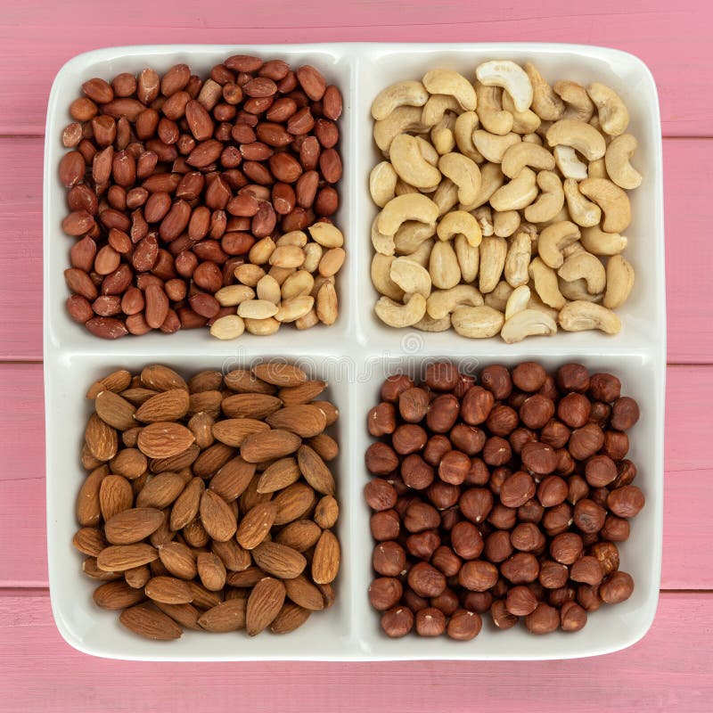 Four kinds of nuts in four compartments on a pink background: stock photos