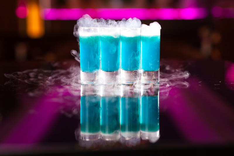 Four light blue cocktail shots with smoke on reflective mirror table stock image Four light blue cocktail shots with smoke on reflective mirror table stock image