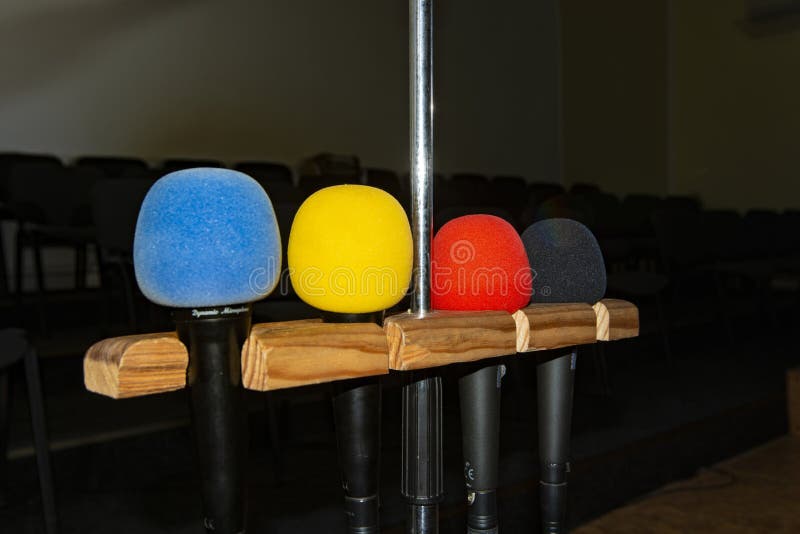Four multi-colored microphones on a stand in an empty room with chairs without people royalty free stock photo Four multi-colored microphones on a stand in an empty room with chairs without people royalty free stock photo
