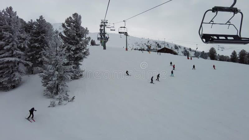 Four person ski chair lift going up a snowy mountain with skiers below stock video