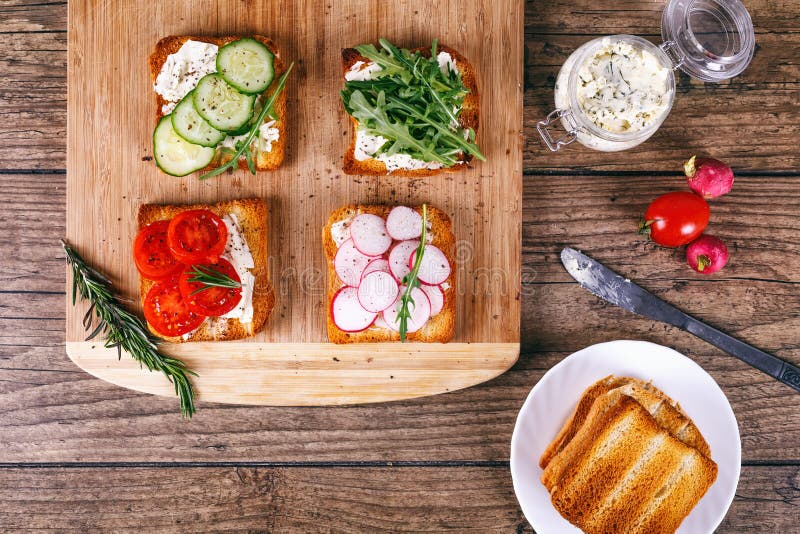 Four sandwiches with fresh vegetables, tomatoes, cucumbers, radish and arugula on a wooden background. Homemade butter