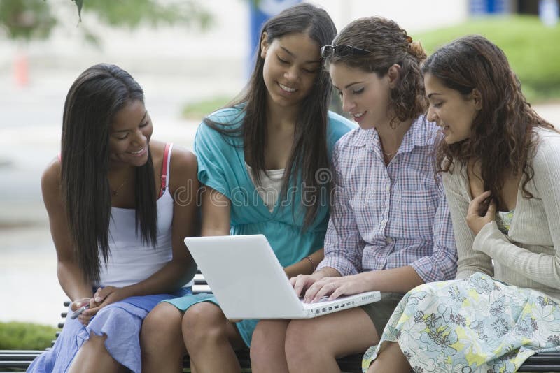 Teenage girl using a laptop with her friends sitting beside her and smiling. Top smiling cheerful stock images, royalty-free photos and pictures