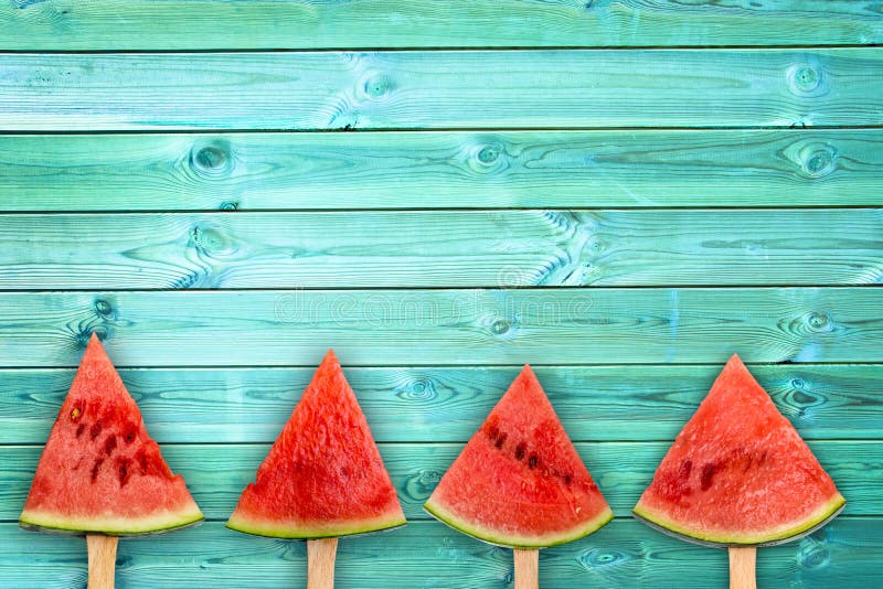 Four watermelon slice popsicles on blue wood background with copy space, fresh summer fruit concept. Four watermelon slice popsicles on blue wood background with copy space, fresh summer fruit concept