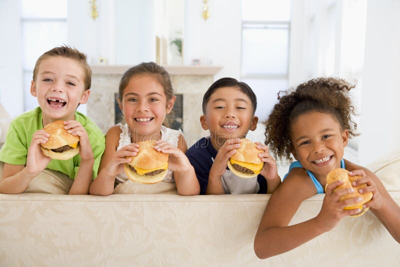 Four young children eating cheeseburgers in living room