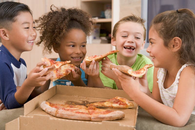 Four young children indoors eating pizza smiling