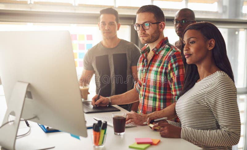 Group of four Black, Caucasian and Hispanic adult entrepreneurs wearing casual clothing while standing around computer for demonstration or presentation. Computer editing stock images, royalty-free photos and pictures