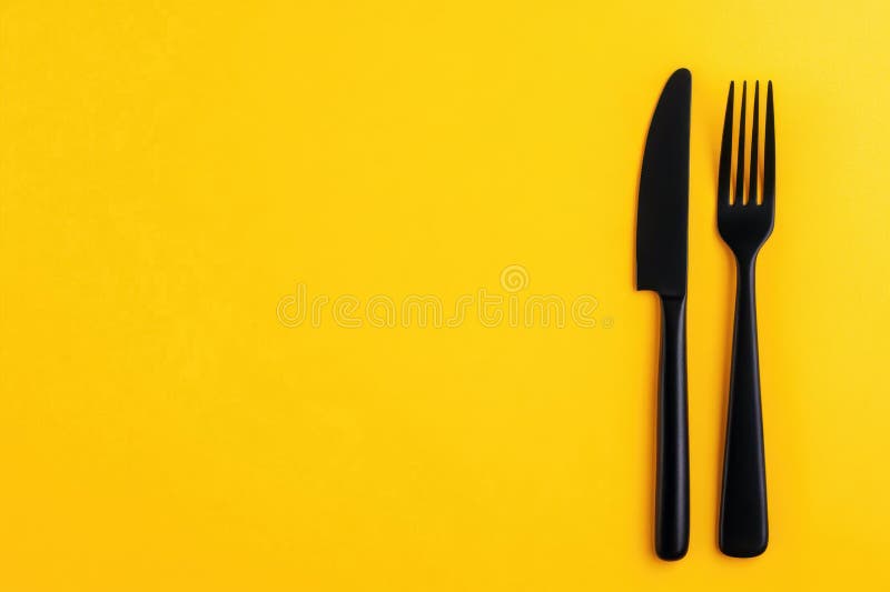 Fourchette noire et couteau disposés sur fond jaune vif dans un cadre minimaliste photos stock