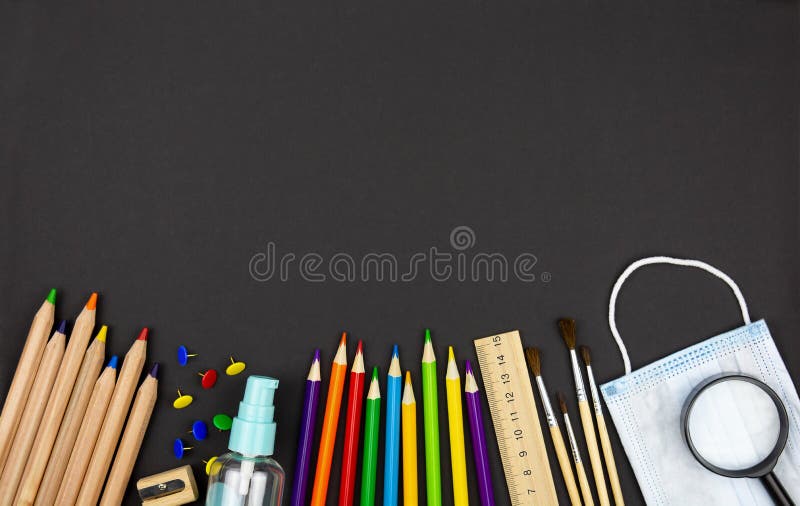 School stationery supplies and COVID-19 prevention items medical mask and hand sanitizer on chalkboard background. Back to school and new normal concept. Top view with copy space. School stationery supplies and COVID-19 prevention items medical mask and hand sanitizer on chalkboard background. Back to school and new normal concept. Top view with copy space