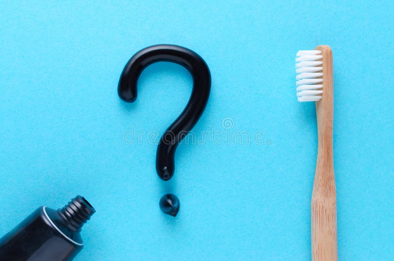 Frage von der schwarzen Zahnpasta, Zähne interessieren sich Konzept, hölzerne Zahnbürste auf blauem Hintergrund stockfotos