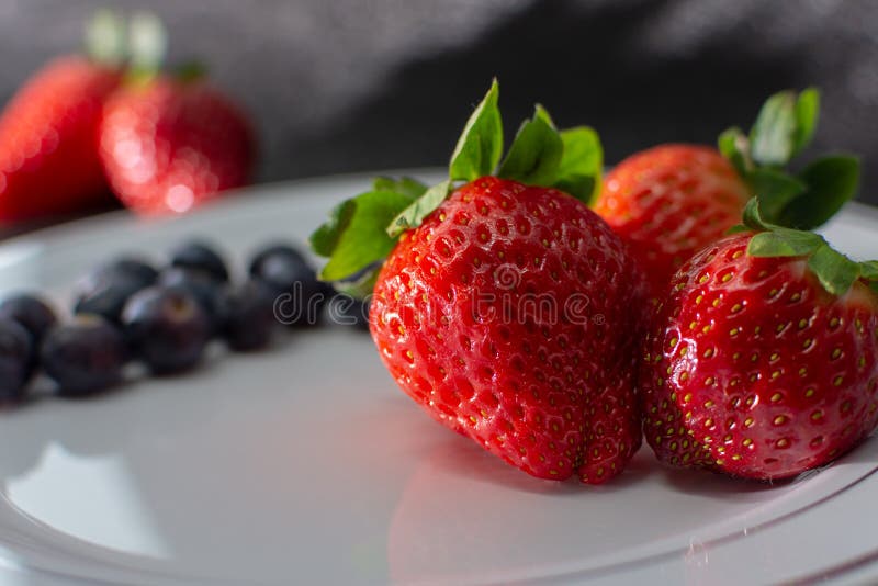 FRAGOLE FRESCHE E PANINI TAGLIATI IN PIATTO BIANCO SU FONDO NERO fotografia stock libera da diritti FRAGOLE FRESCHE E PANINI TAGLIATI IN PIATTO BIANCO SU FONDO NERO fotografia stock libera da diritti