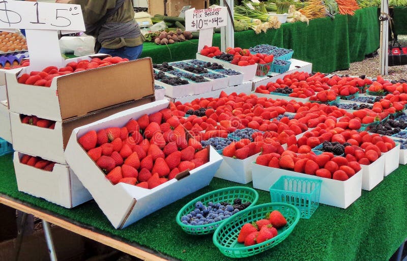 This is an image of boxes of strawberries and blueberries on display in a small town Farmer`s Market.  There are other tables with more produce on display for shoppers.  There is a table of different types of vegetables in the background.  There are beets, green onions, carrots and other root vegetable on display.  There are handmade signs with price written on them and a carton of brown chickens eggs at the far left.  This image could be used to represent local commerce, capitalism, trade, farms, farming, shopping, country life, small town america, community.  this image could be used as background or screen saver. This is an image of boxes of strawberries and blueberries on display in a small town Farmer`s Market.  There are other tables with more produce on display for shoppers.  There is a table of different types of vegetables in the background.  There are beets, green onions, carrots and other root vegetable on display.  There are handmade signs with price written on them and a carton of brown chickens eggs at the far left.  This image could be used to represent local commerce, capitalism, trade, farms, farming, shopping, country life, small town america, community.  this image could be used as background or screen saver.