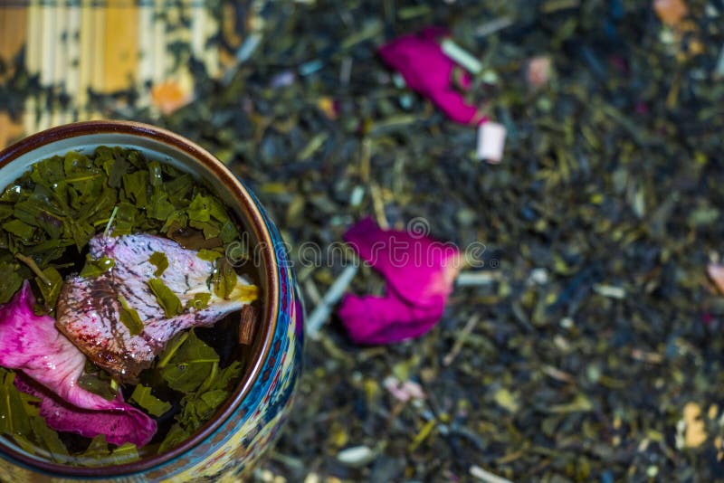 Fragrant green tea with red rose petals brewed in a cup with ornaments of Chinese culture.