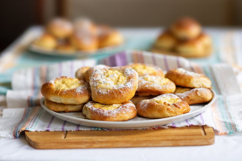 Fragrant mouth-watering buns stuffed with cheese. Homemade dessert on a plate, tablecloth and wooden cutting board. Shallow depth of field stock image Fragrant mouth-watering buns stuffed with cheese. Homemade dessert on a plate, tablecloth and wooden cutting board. Shallow depth of field stock image