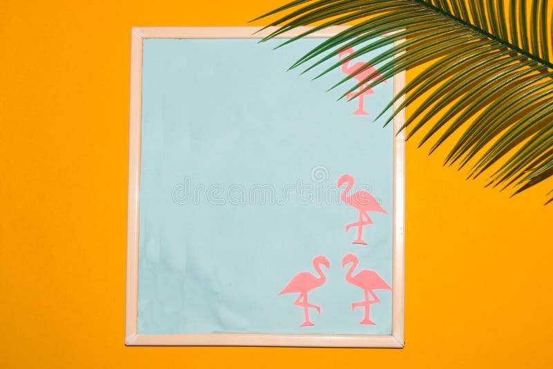Frame with blue copy space and paper flamingos around the frame yellow background with palm leaf, creative summer design royalty free stock photo