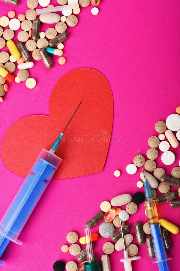 Frame made of round pills and capsules put parallelly. Set of colorful pills scattered on pink background, copy space. Drugs near heart with blue syringe. Heart disease and medicine concept