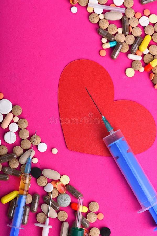 Frame made of round pills and capsules put parallelly. Set of colorful pills scattered on pink background, copy space. Drugs near heart with blue syringe. Heart disease and medicine concept