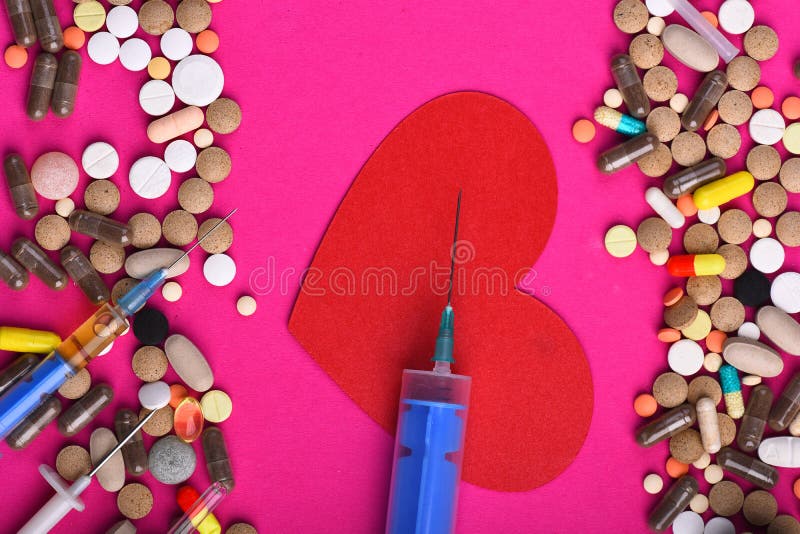 Frame made of round pills and capsules put on sides. Set of colorful pills scattered on pink background, copy space. Heart disease and medicine concept. Drugs near heart with blue syringe