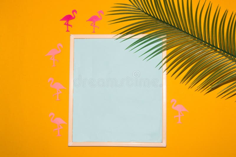 Frame with pastel blue copy space around the frame yellow background with flamingos and palm leaf, creative summer concept stock image