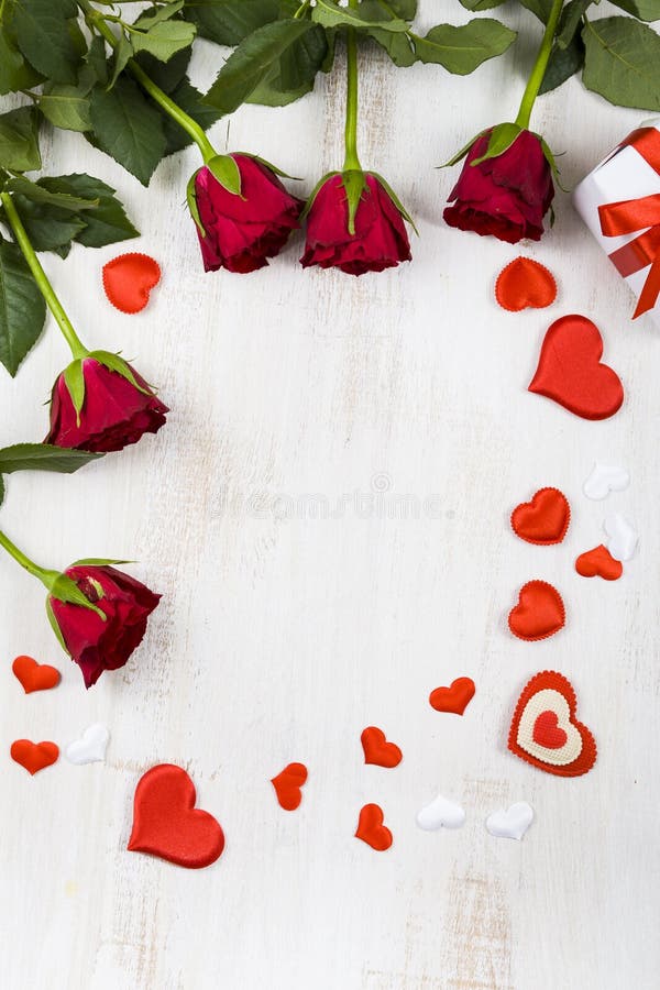 Frame of red roses and hearts on a wooden background.