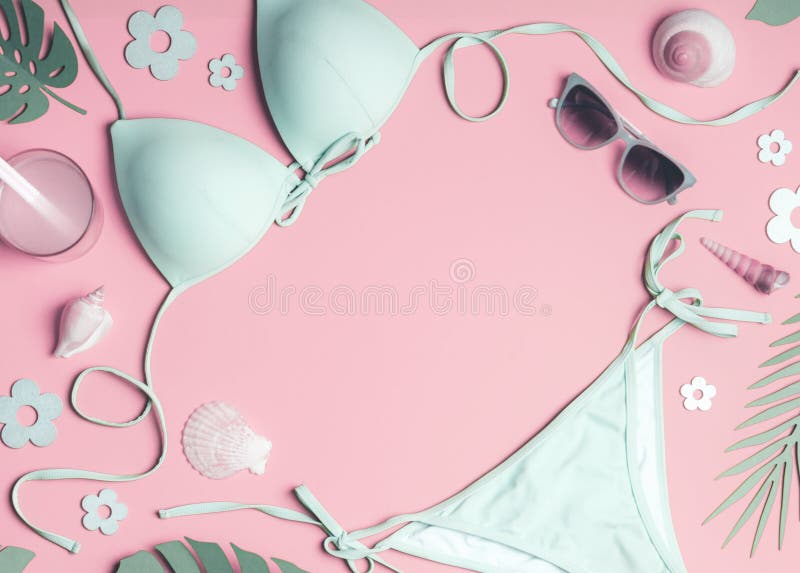 Frame of woman beach accessories: bikini, sun hat, sandals, sunglasses and bag, sea shells and tropical leaves on pastel pink