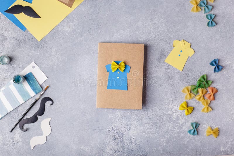 Framställning av hälsningkortet för faderdag Skjorta med fjärilen från pasta Kort från papper moustache Barns konstprojekt royaltyfria bilder Framställning av hälsningkortet för faderdag Skjorta med fjärilen från pasta Kort från papper moustache Barns konstprojekt royaltyfria bilder