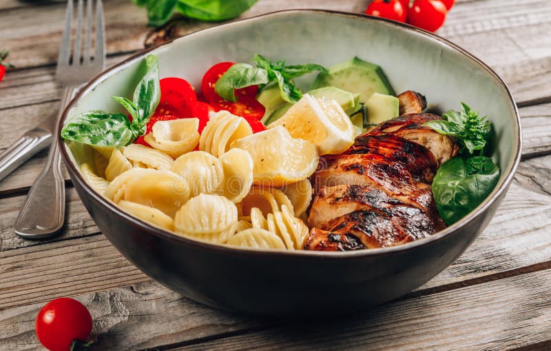 Frango grelhado com massa orecchiette, tomate fresco e folhas de manjericão imagem de stock