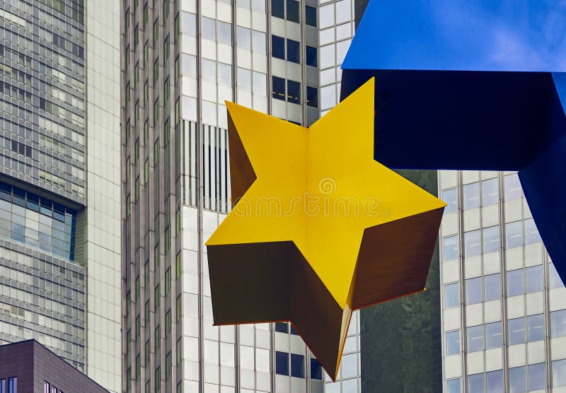 Frankfurt, Germany, October 2., 2019: Detail of a yellow star of the Euro sculpture with the old former building of the European Central Bank ECB in the background