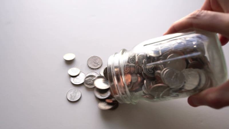 Frasco de monedas derramando monedas estadounidenses a cámara lenta sobre una superficie brillante almacen de video