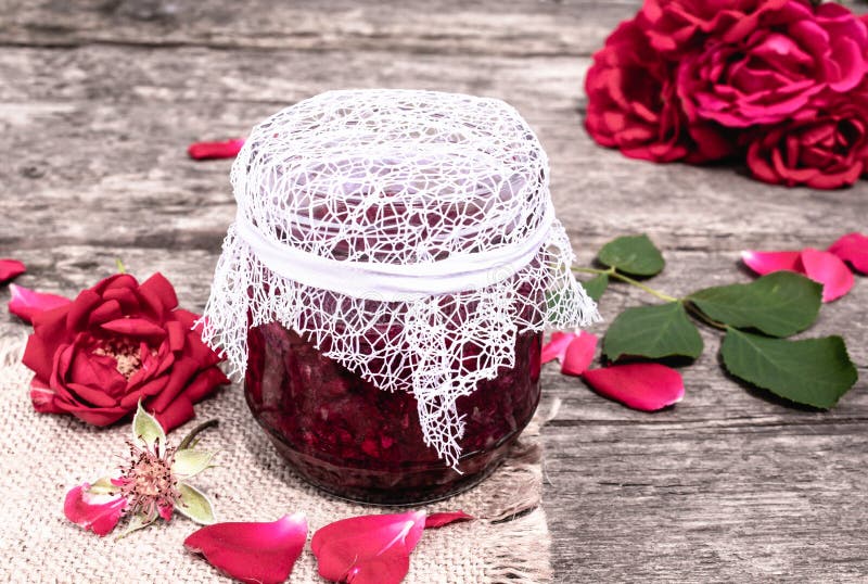 Frasco do doce das pétalas cor-de-rosa em uma tabela de madeira com as flores das rosas Confiture da flor Alimento saud?vel fotografia de stock Frasco do doce das pétalas cor-de-rosa em uma tabela de madeira com as flores das rosas Confiture da flor Alimento saud?vel fotografia de stock