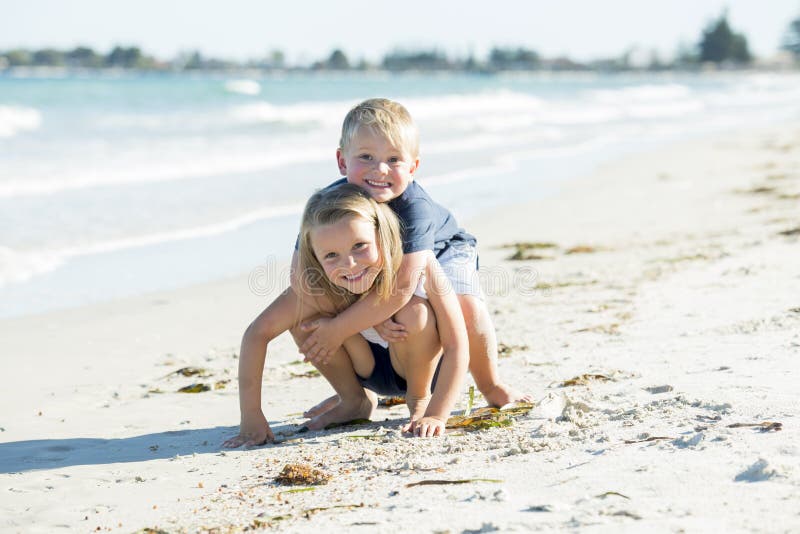 Fratelli germani poco adorabili e dolci che giocano insieme in spiaggia di sabbia con il piccolo fratello che abbraccia il suo be fotografia stock Fratelli germani poco adorabili e dolci che giocano insieme in spiaggia di sabbia con il piccolo fratello che abbraccia il suo be fotografia stock