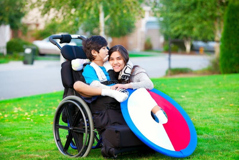 Fratello disabile che abbraccia sorella più anziana in sedia a rotelle all'aperto fotografia stock