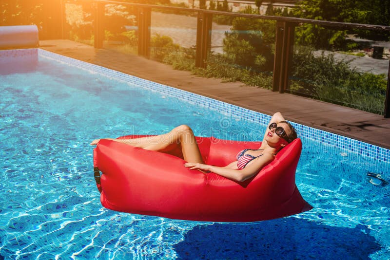 Frau auf rotem Ruhesessel im Pool stockfotografie Frau auf rotem Ruhesessel im Pool stockfotografie