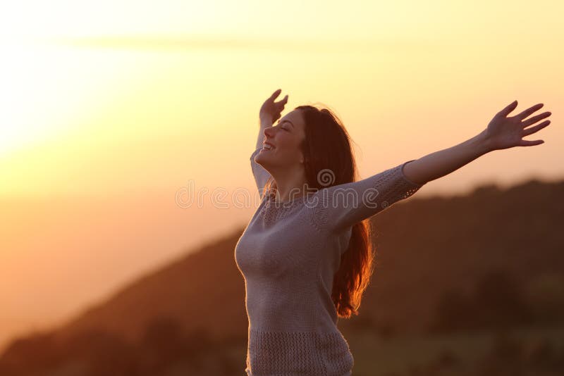 Frau bei dem Sonnenuntergang, der die Frischluft anhebt Arme atmet