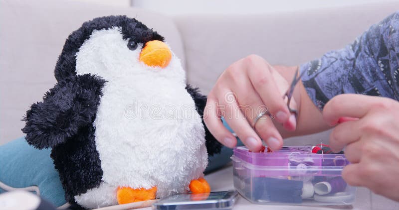 Frau bereitet Nähzubehör vor, um den Pinguin mit zerrissenem Pinguin zu fixieren