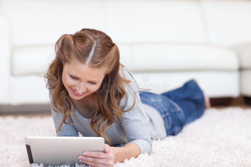 Frau, die auf den Teppich bei der Anwendung ihrer Tablette legt lizenzfreie stockbilder Frau, die auf den Teppich bei der Anwendung ihrer Tablette legt lizenzfreie stockbilder