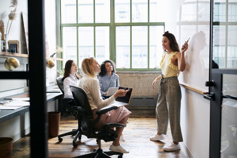 Frau, die auf whiteboard in einer Sitzung mit weiblichem Team zeigt stockbilder