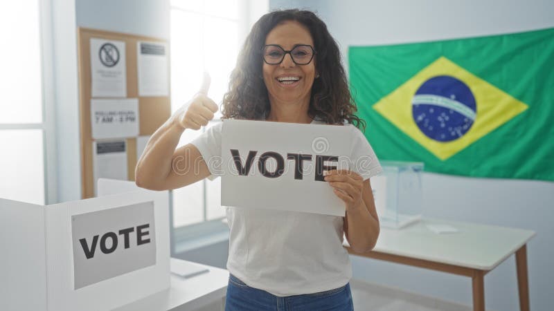 Frau, die in einem brasilianischen Wahllokal abstimmt und ein Stimmzeichen trägt und eine Daumenschraube mit einer Fahne im Hinter stockfoto