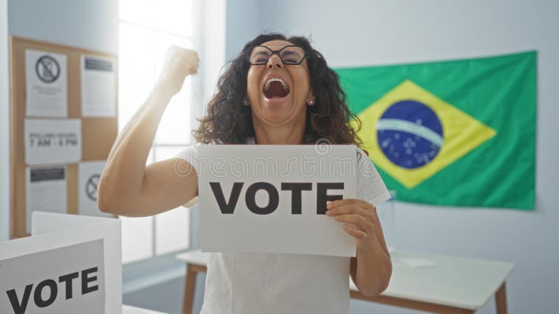 Frau, die an einem Wahllokal mit einem Wahlzeichen mit brasilianischer Flagge im Hintergrund feiert lizenzfreie stockfotografie