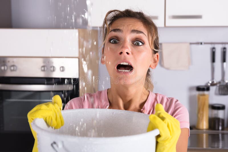 Frau, die einen Eimer hält, während Wasser-Tröpfchen von der Decke lecken stockfotos Frau, die einen Eimer hält, während Wasser-Tröpfchen von der Decke lecken stockfotos