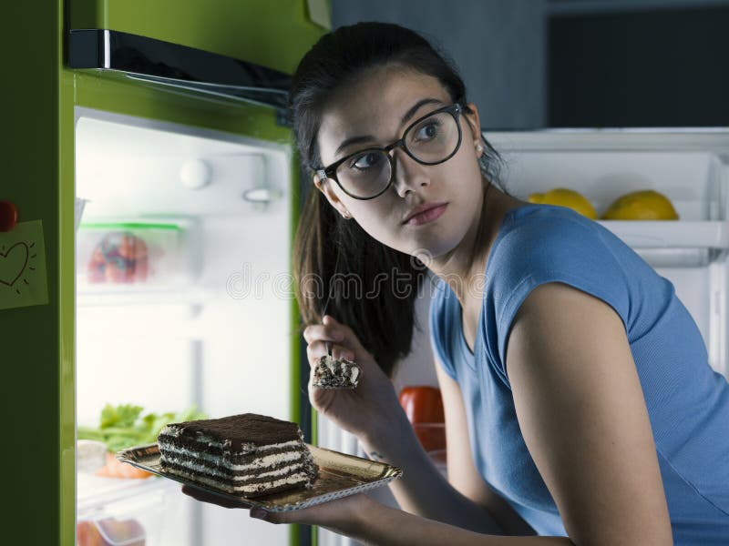 Woman in the kitchen having a late night snack, she is taking a delicious dessert from the fridge, diet fail concept. Woman in the kitchen having a late night snack, she is taking a delicious dessert from the fridge, diet fail concept