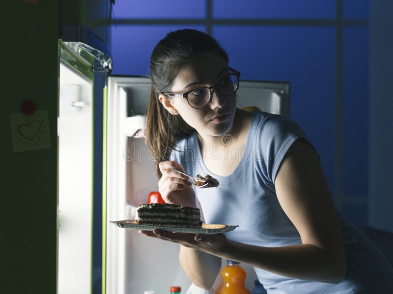 Woman in the kitchen having a late night snack, she is taking a delicious dessert from the fridge, diet fail concept. Woman in the kitchen having a late night snack, she is taking a delicious dessert from the fridge, diet fail concept