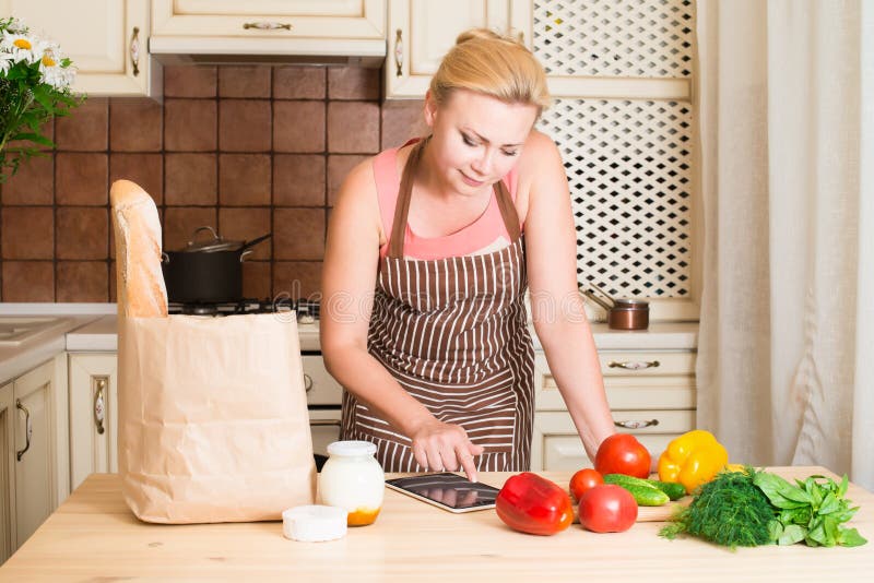 Frau, die einen Tablet-Computer verwendet, um in ihrer Küche zu kochen stockfotografie Frau, die einen Tablet-Computer verwendet, um in ihrer Küche zu kochen stockfotografie