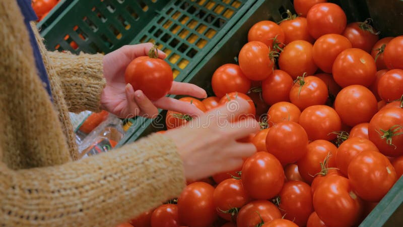 Frau, die frische rote Tomaten am Gemischtwarenladen kauft