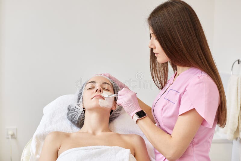 Frau, die Gesichtspflege durch Kosmetiker am Badekurortsalon erhält Cosmetologist befeuchtende Maske auf weiblichem Gesicht von d stockfotos Frau, die Gesichtspflege durch Kosmetiker am Badekurortsalon erhält Cosmetologist befeuchtende Maske auf weiblichem Gesicht von d stockfotos
