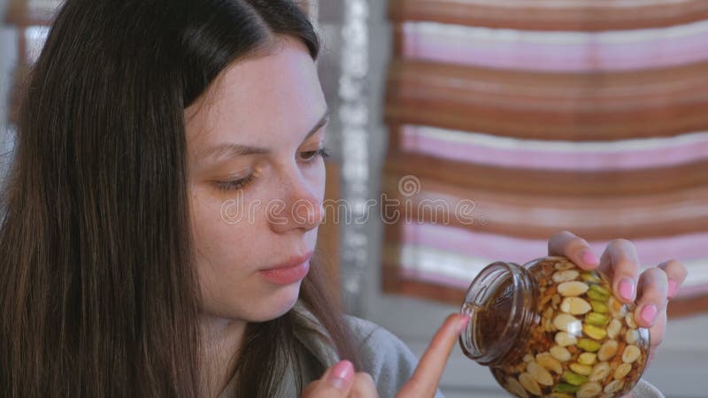 Frau, die Honig von einem Glas Nüssen im Honig mit dem Finger isst