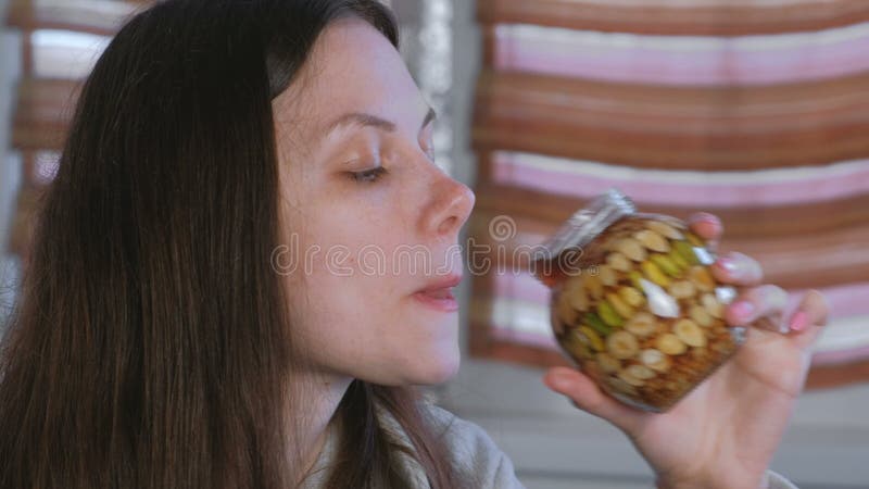 Frau, die Honig von einem Glas Nüssen im Honig mit dem Finger isst